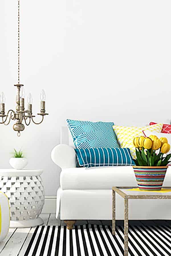 white sofa with colourful pillows, chandelier, and pot of yellow tulips all depicting how to live hygge in spring