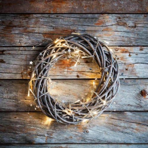 grapevine wreath hanging on a barn wall with fairy lights wrapped around it