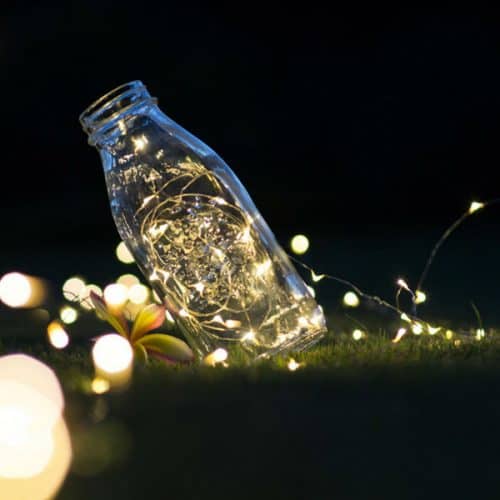 milk bottle with string fairy lights inside at night on green grass