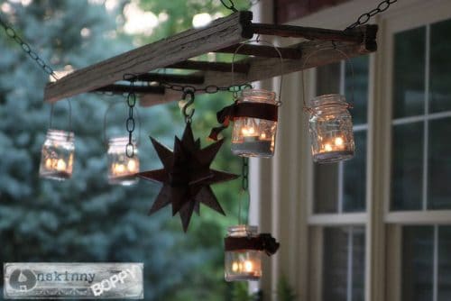 a ladder chandelier and tin star shows clear glass jars hanging from ladder and lights in inside next to a building