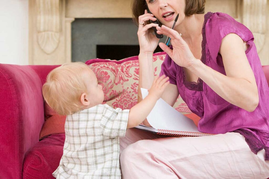 woman on phone with planner and pen in hand shows small child reaching out for her