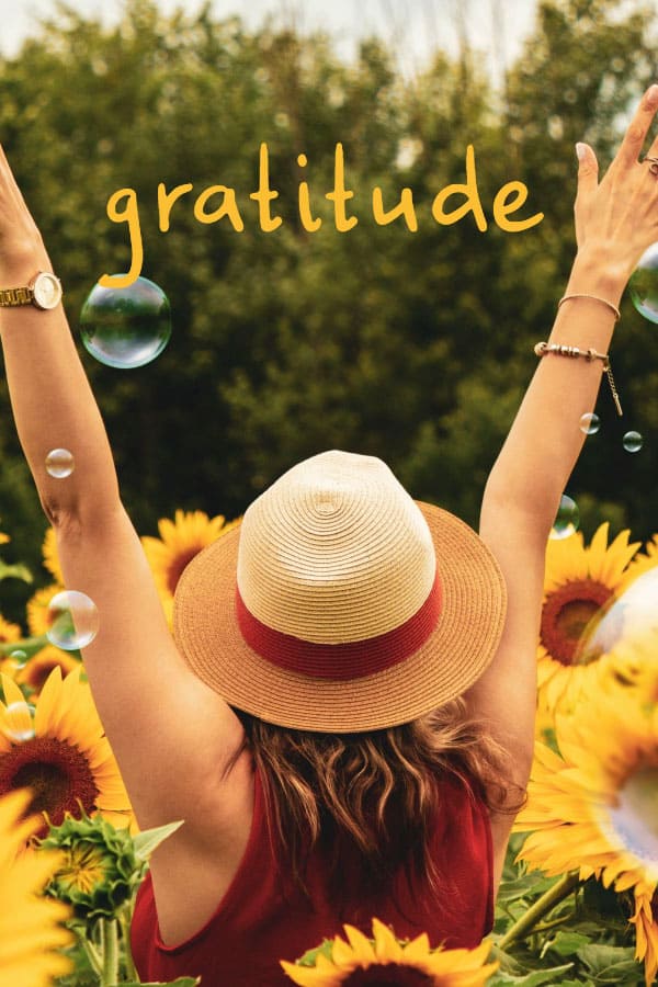 woman wearing a straw hat with arms outstretched standing in a field of sunflowers. text says gratitude in yellow type, with bubbles floating around here, and her back is to the camera 