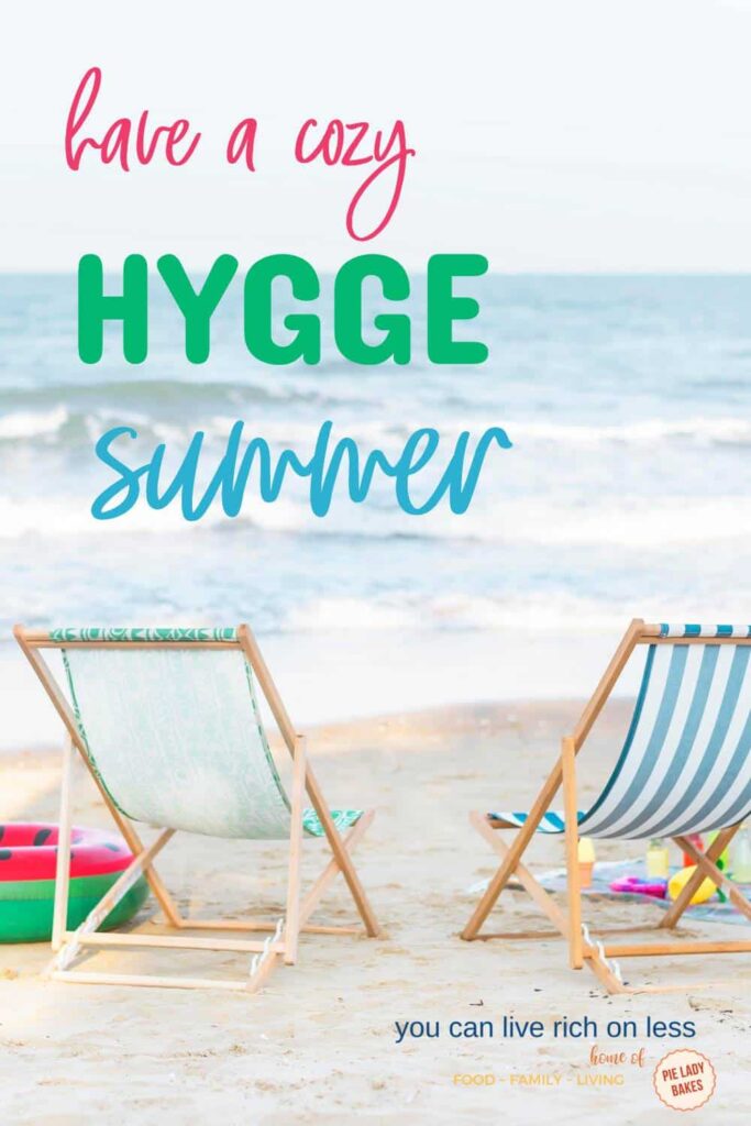 two beach chairs on the sand with ocean in front beach toys in background text says have a cozy hygge summer