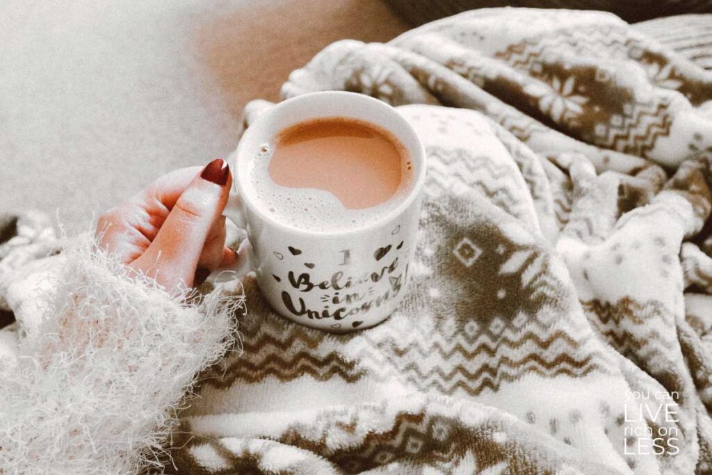 arm in cozy sweater holding a cup of coffee person is wrapped in cozy blankets