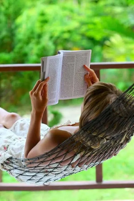 A woman reading a book while laying in a hammock